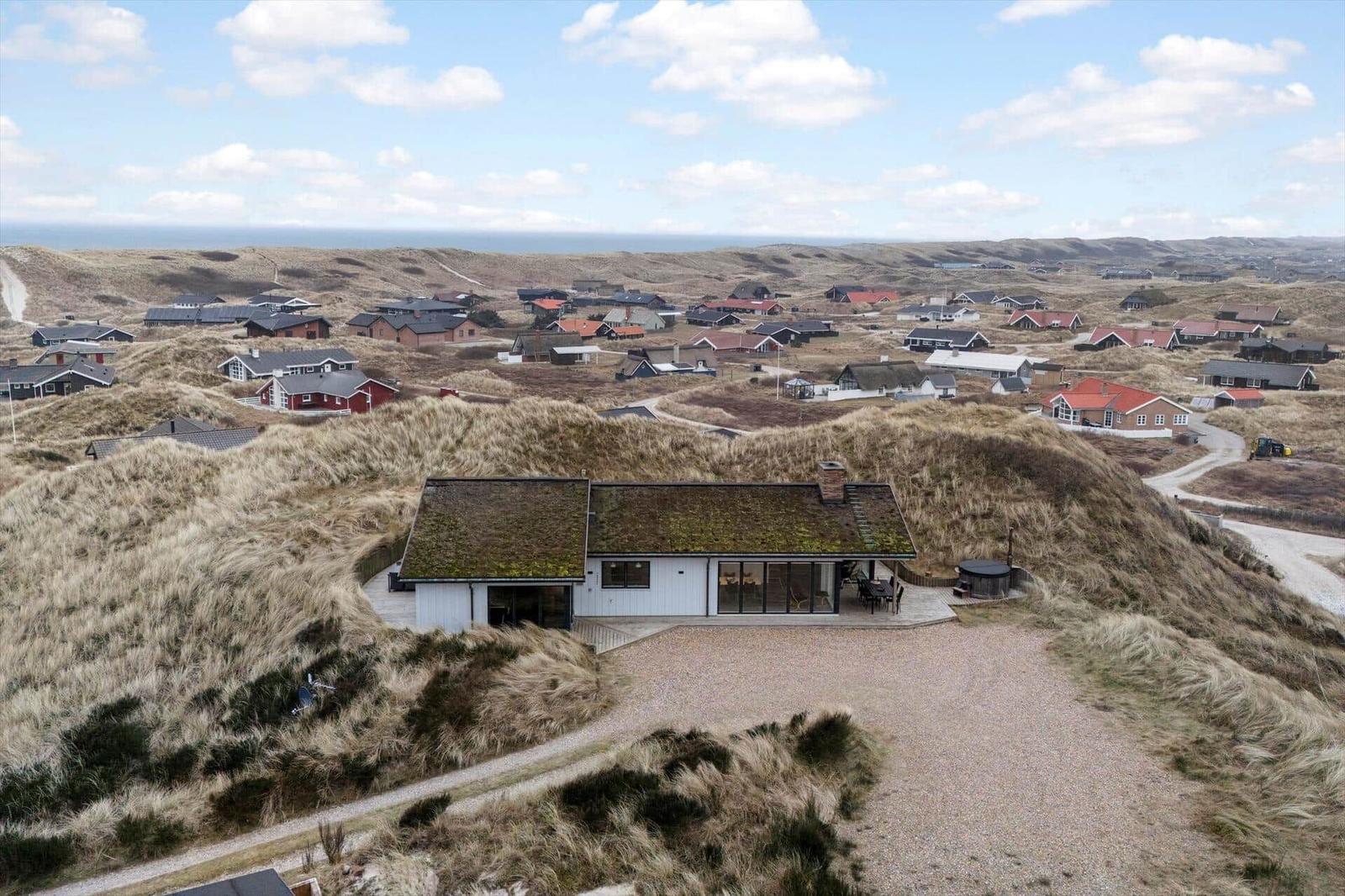 Moderne Villa mit Grasdach auf Dünen, Blick auf Küstenlandschaft mit Häusern.