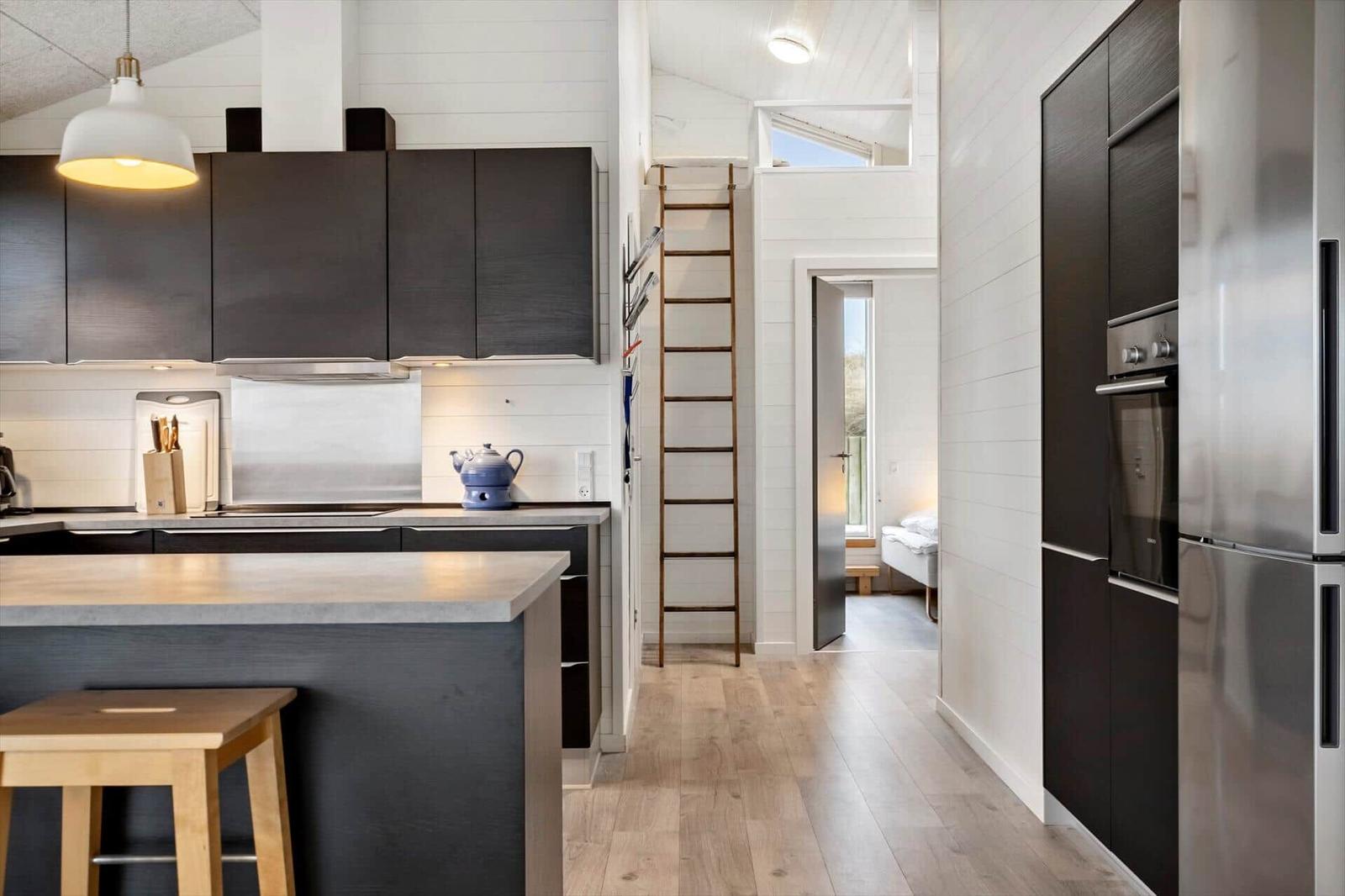 Küche mit dunklen Schränken, Edelstahlgeräten und Holzboden. Treppe führt zum Dachboden.