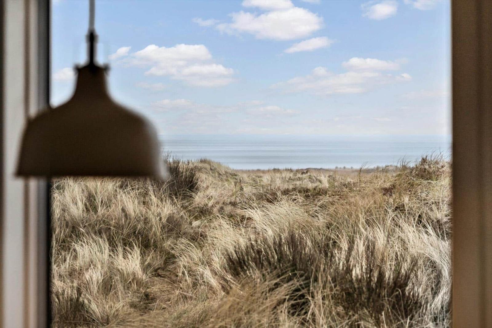 Durch das Fenster sieht man das Meer und trockenes Gras.