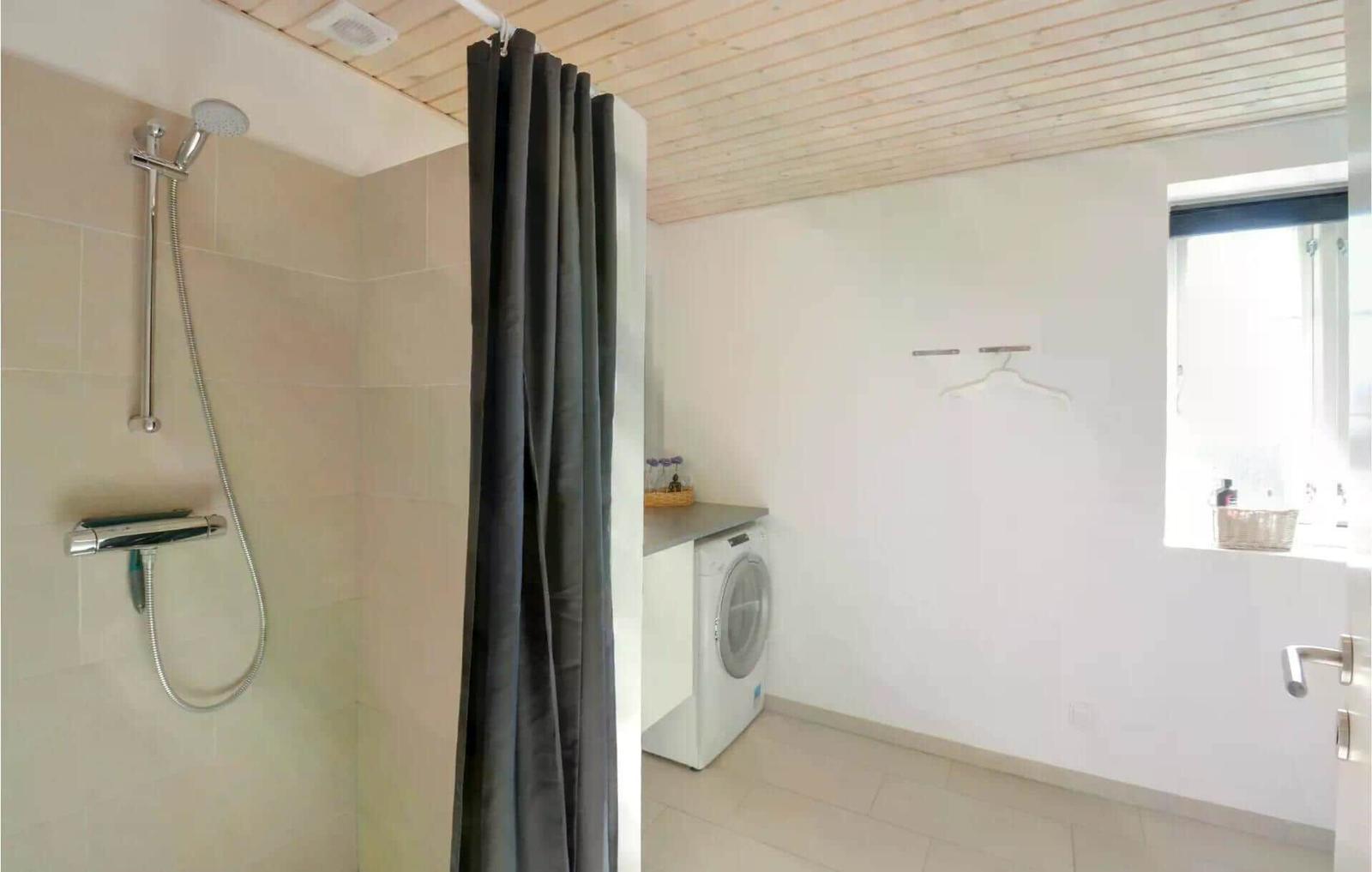 Dusche mit Duschbrause, Waschmaschine und Fenster.