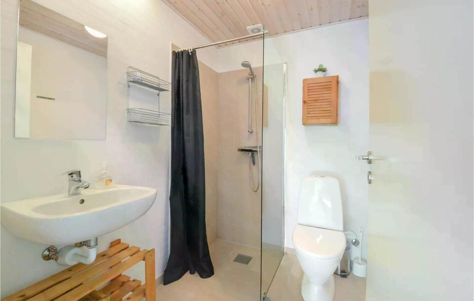 Badezimmer mit Dusche, Toilette und Waschbecken auf Holzgestell.