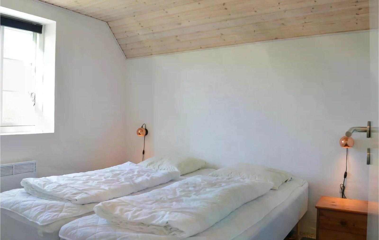 Zimmer mit Doppelbett, Holzdecke und Fenster. Beide Betten sind mit weißen Bettwäschen bezogen.