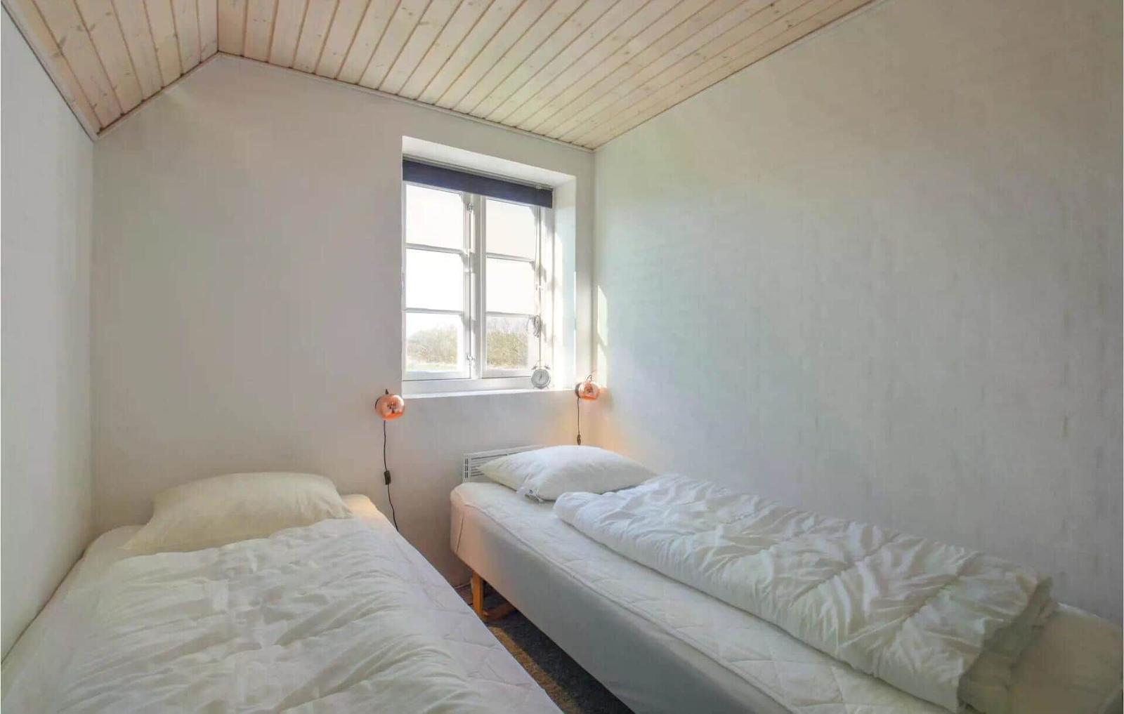 Zwei Einzelbetten unter einem Holzdach mit Fenster und Wandlampen.