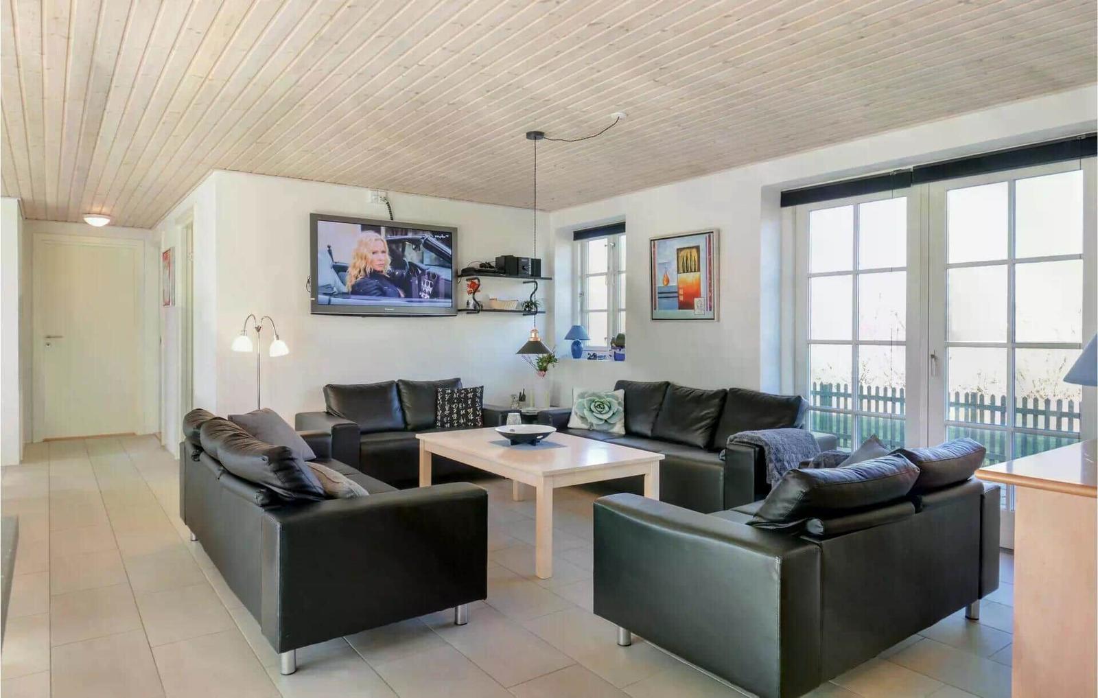 Wohnzimmer mit schwarzen Ledermöbeln, Fernseher und Fenstern.