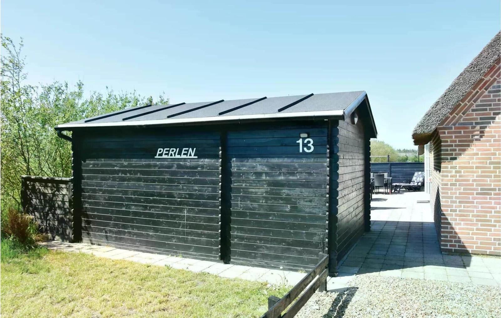 Schwarzer Holzschuppen mit der Aufschrift PERLEN und der Nummer 13. Neben einem Steinweg und einer Terrasse.