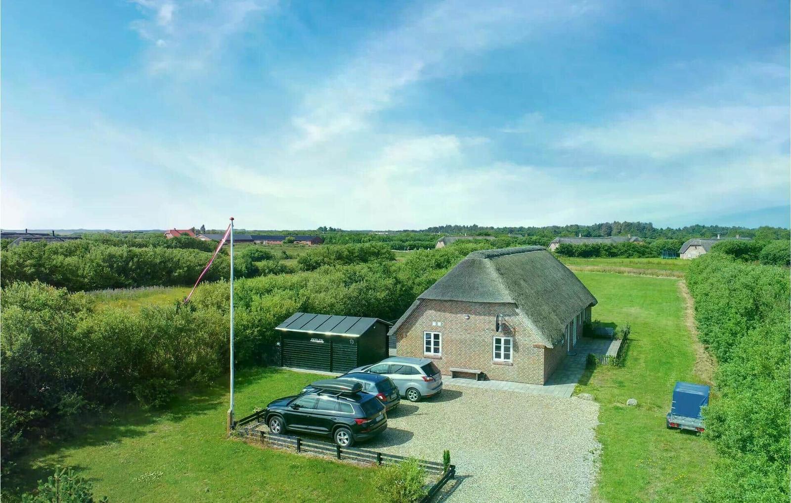 Haus mit Strohdach, Parkplatz und Grünanlagen im ländlichen Umfeld.