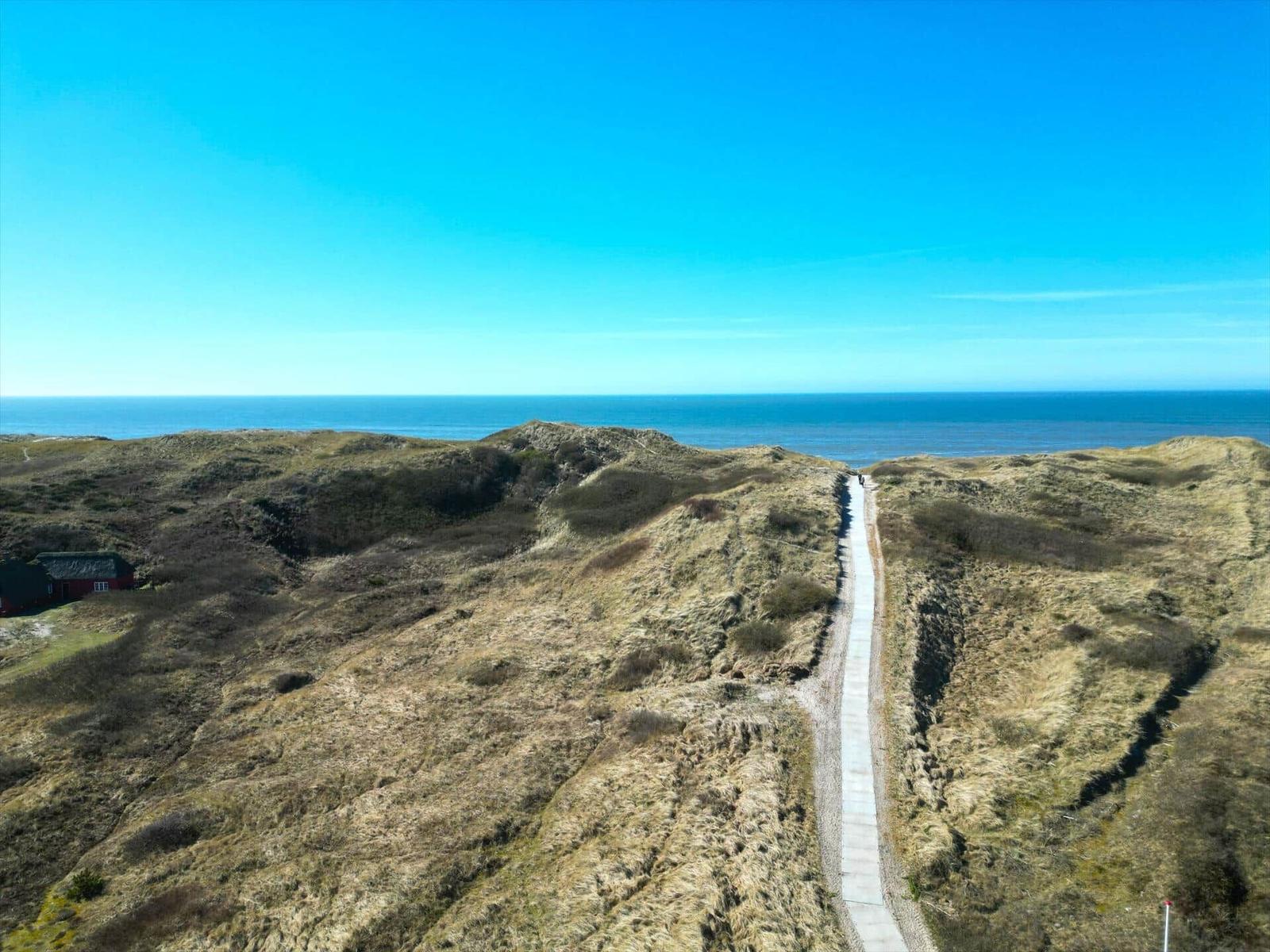 Hügelige Landschaft mit Blick auf das Meer und einem Weg zum Strand.