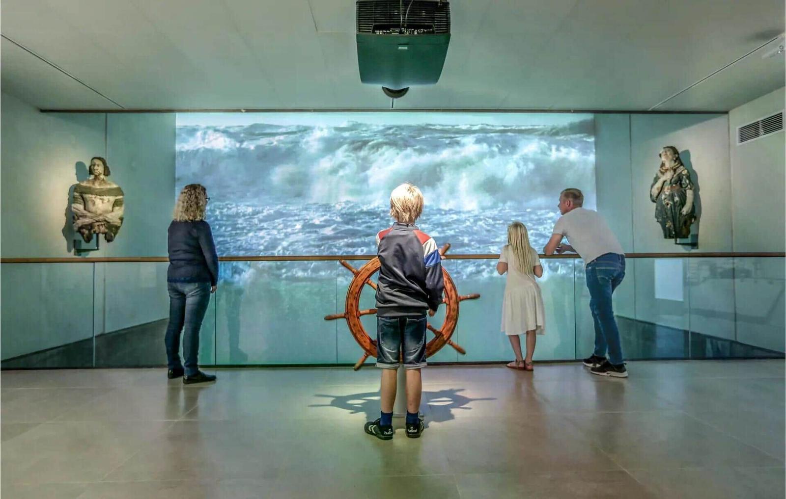 Besucher betrachten eine maritime Projektion mit Ruder und Skulpturen an den Wänden.