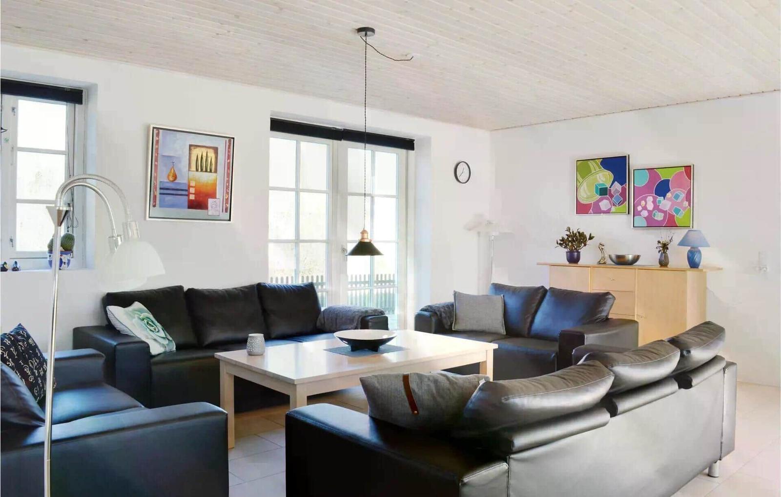 Wohnzimmer mit schwarzen Sofas, weißem Tisch und bunten Bildern an den Wänden.