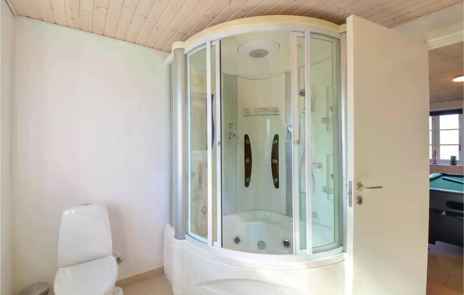 Bad mit Dusche und Toilette. Holzdecke und weißer Fliesenboden.