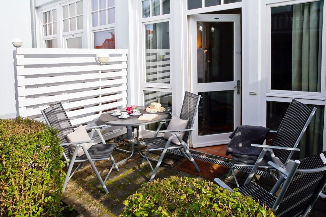 Terrasse mit Tisch, Stühlen und Pflanzen vor weißem Haus