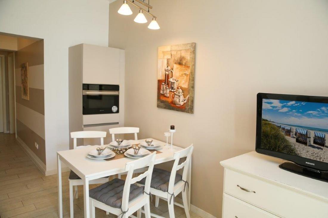 Esszimmer mit Tisch, Stühlen und integriertem Ofen. Fernseher zeigt Strandbild.