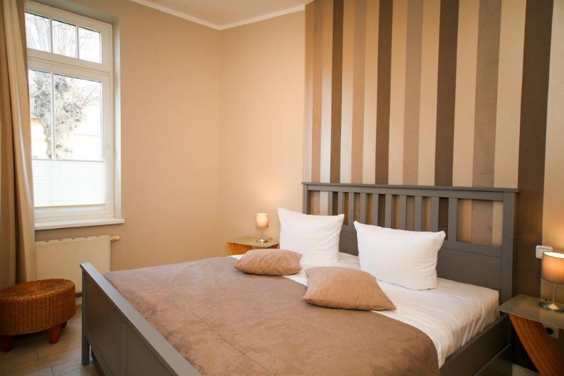 Schlafzimmer mit Bett, Fenster und gestreifter Wandverkleidung.