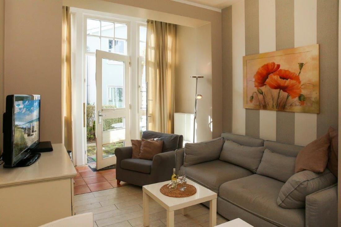 Wohnzimmer mit Sofa, Sessel und TV. Durchgang zur Terrasse mit Blick nach draußen.