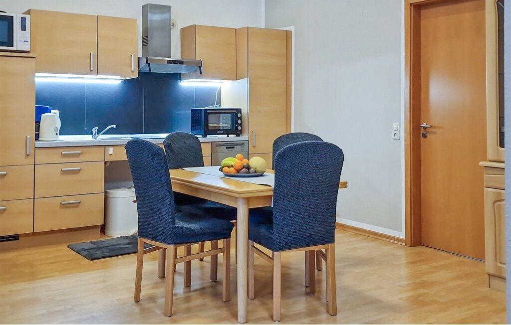 Küche mit Esstisch und vier Stühlen. Hintergrund: Holzschrank, Dunstabzug, Mikrowelle.