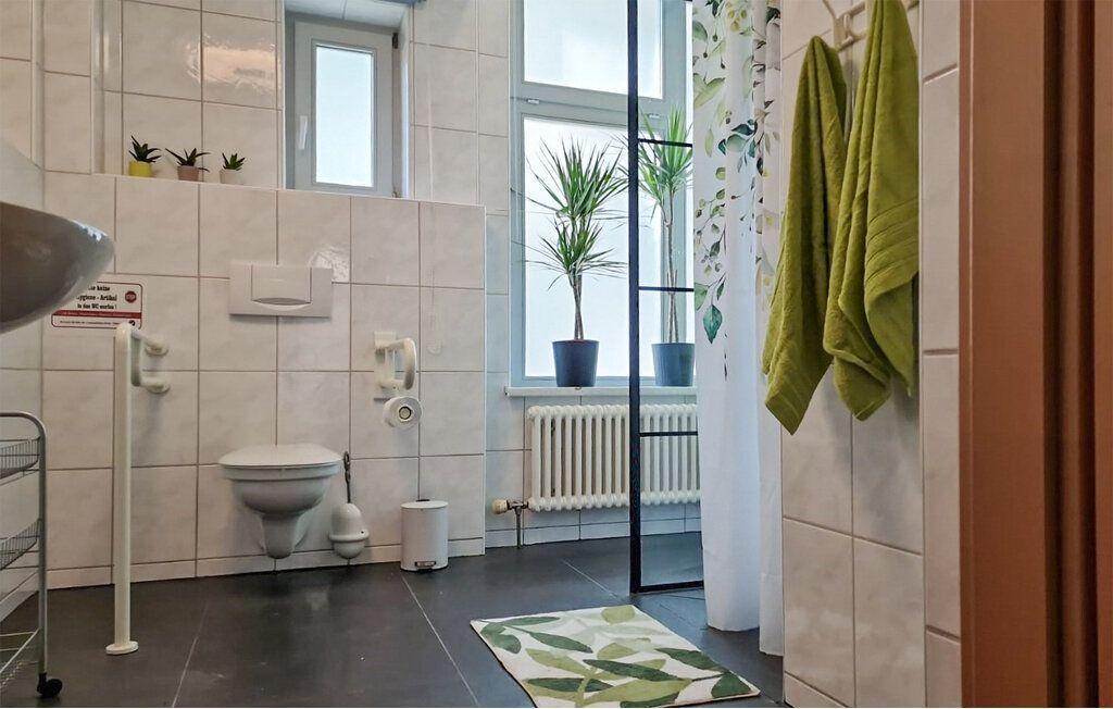 Badezimmer mit Toilette, Waschbecken und Dusche. Grüne Handtücher und Pflanzen im Fenster.