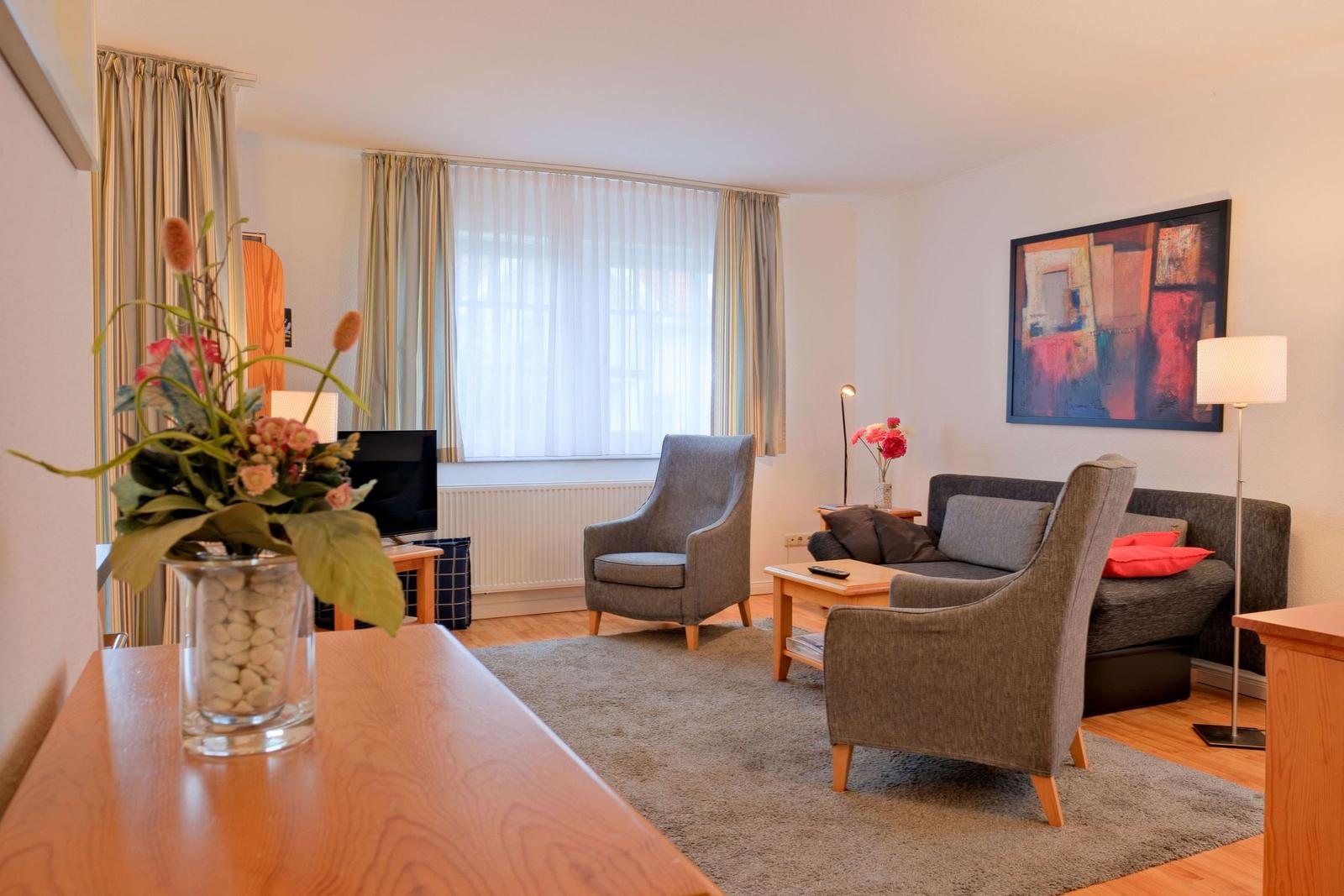 Wohnzimmer mit Sofa, Sessel, Couchtisch und Fenster mit Vorhängen.