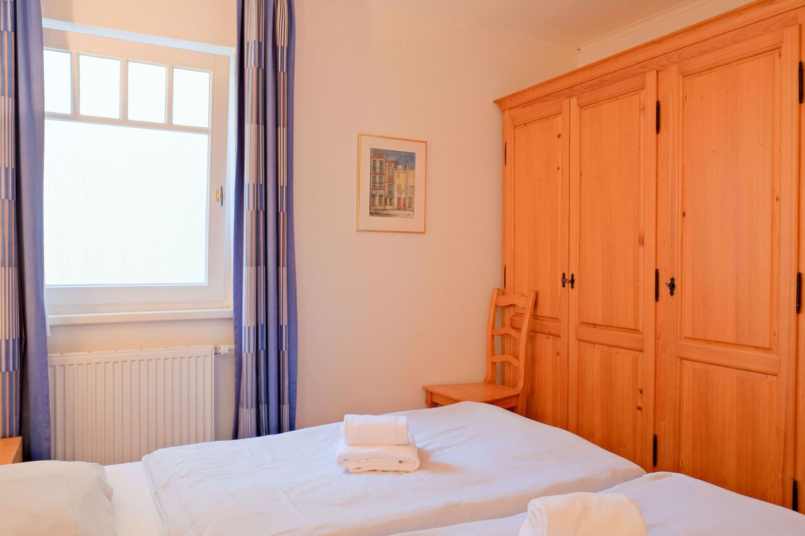 Schlafzimmer mit Doppelbett, Holzschrank und Fenster mit Vorhängen.