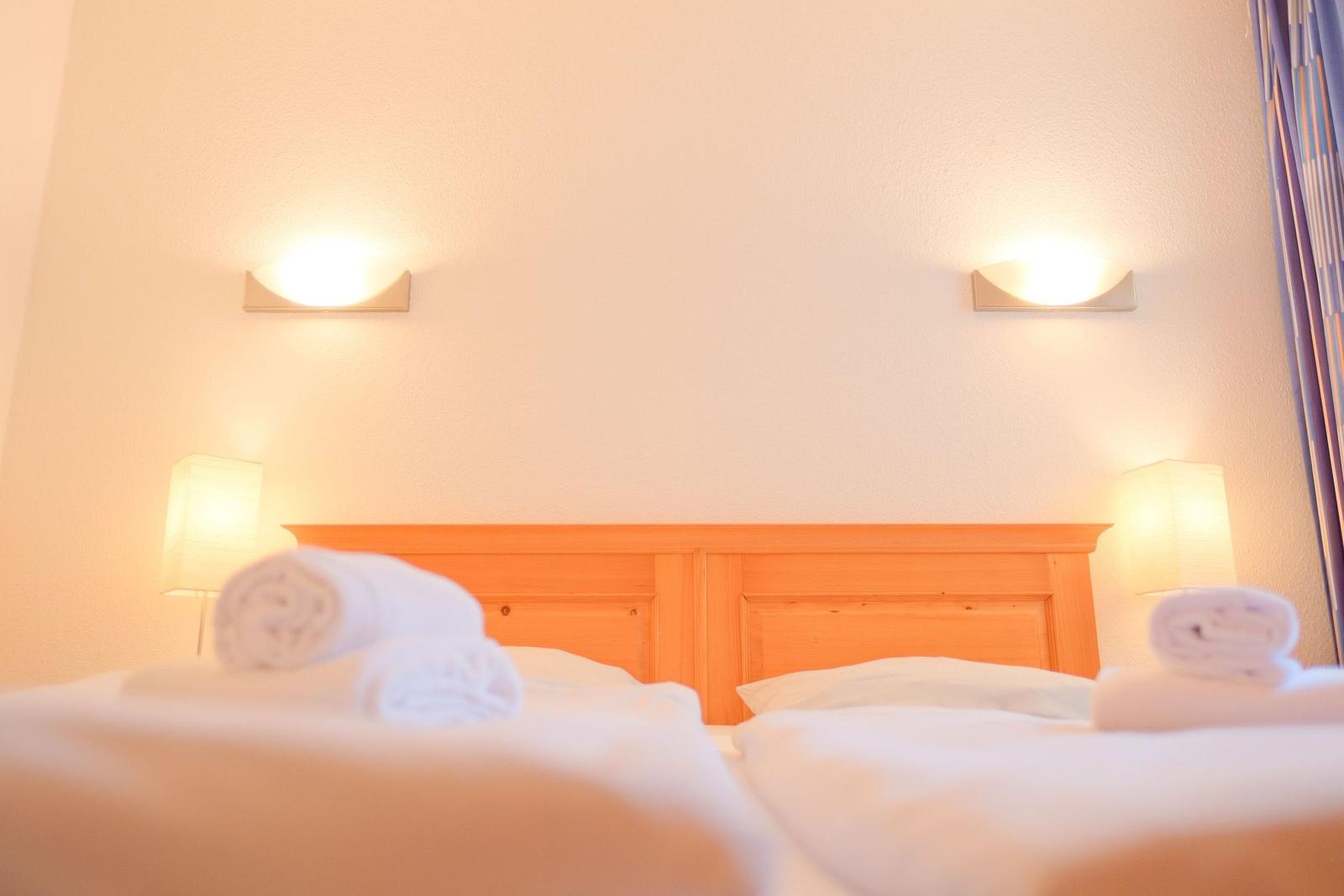 Doppelbett mit Holzrahmen, zwei Wandlampen und gefalteten Handtüchern.