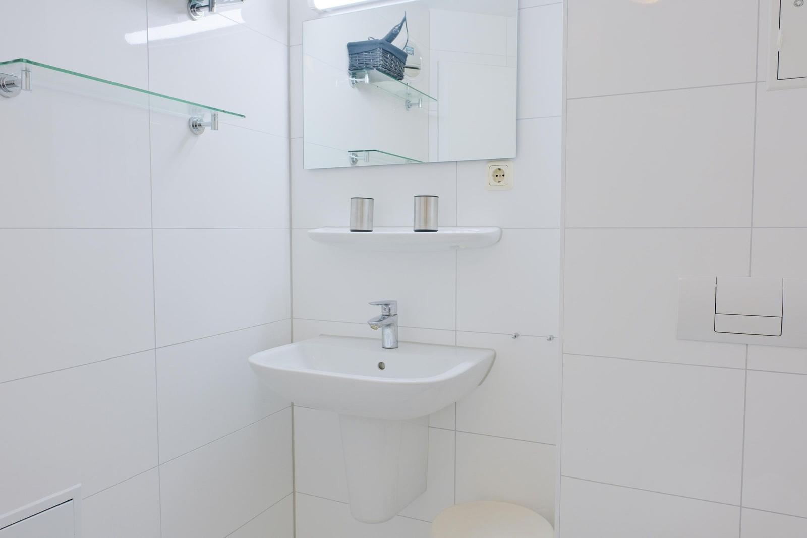 Badezimmer mit Waschbecken, Spiegel und Glasregal an der Wand.