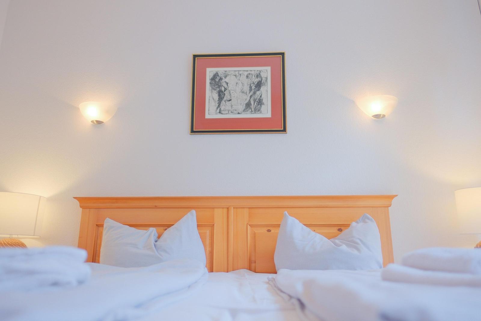 Schlafzimmer mit Holzbett, weißen Kissen und Wandbild.