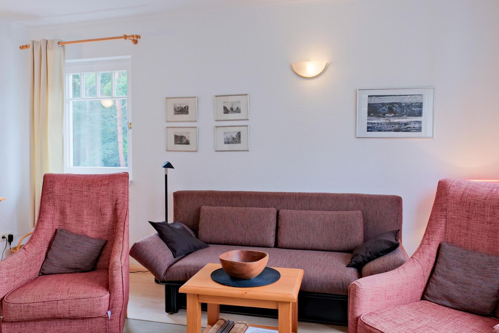 Ein Wohnzimmer mit Sofa und zwei Sesseln, Tisch und Fenster.