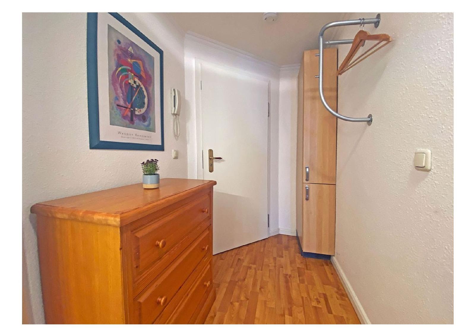 Flur mit Holzschrank, Kleiderständer und Schminktisch mit Bild an der Wand.