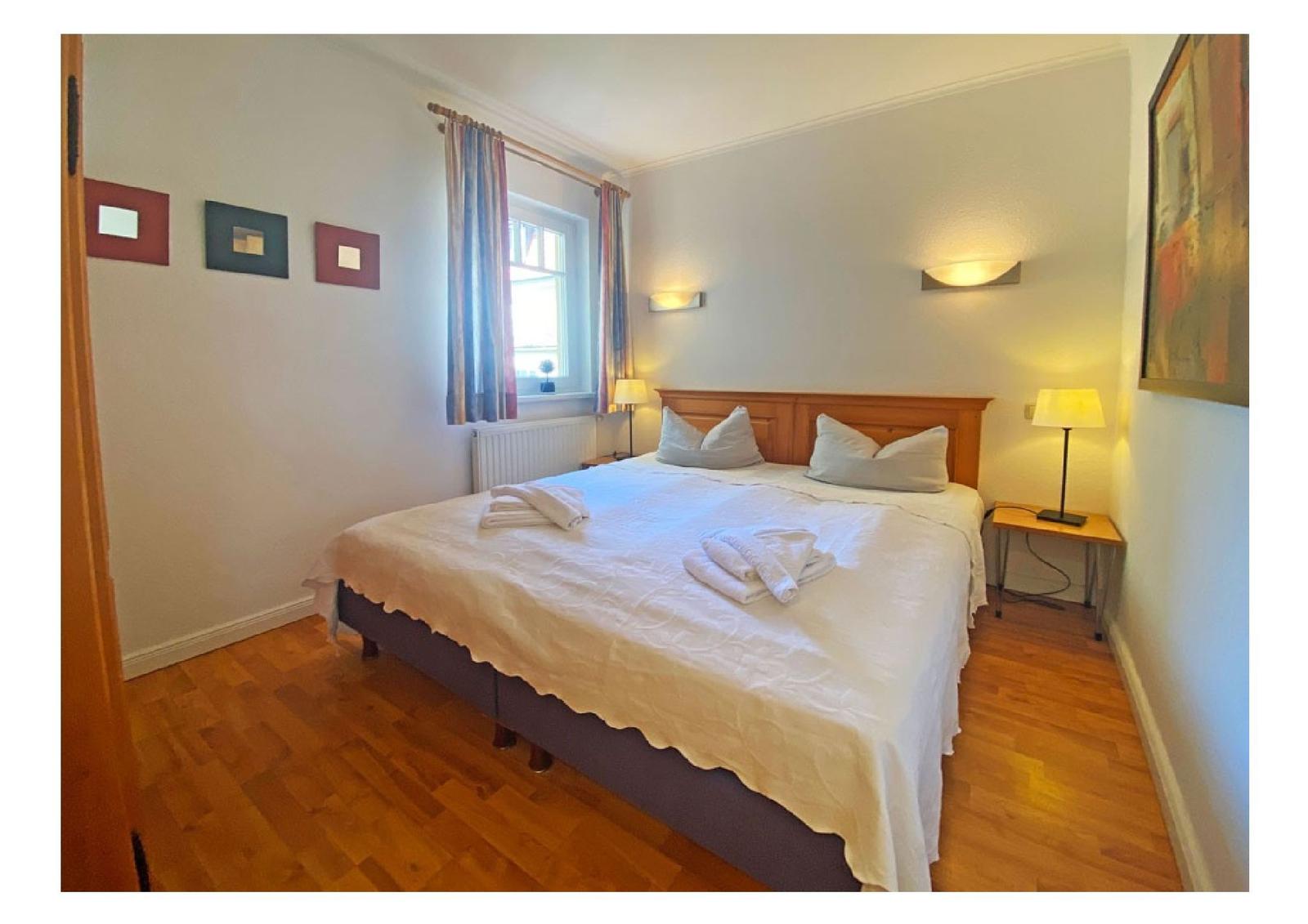 Schlafzimmer mit Doppelbett, Holzboden und Fenster mit Vorhängen.