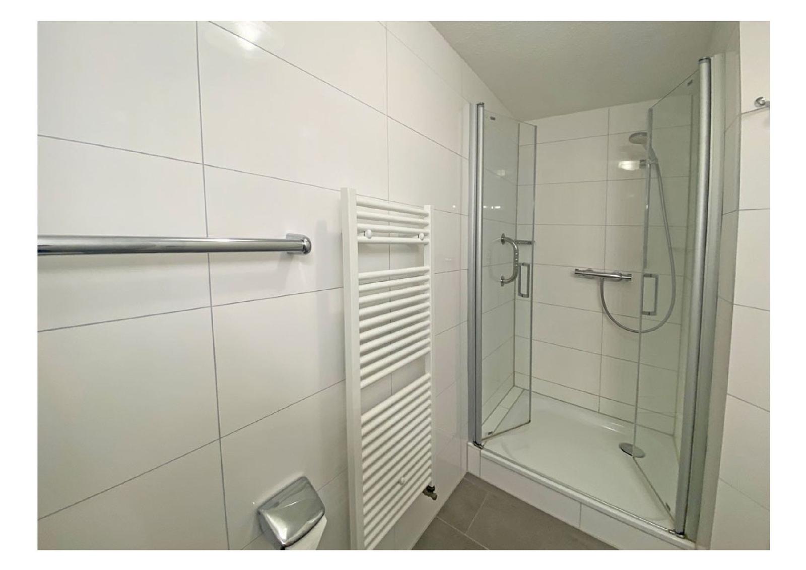 Badezimmer mit Dusche, Heizkörper und Handtuchhalter.