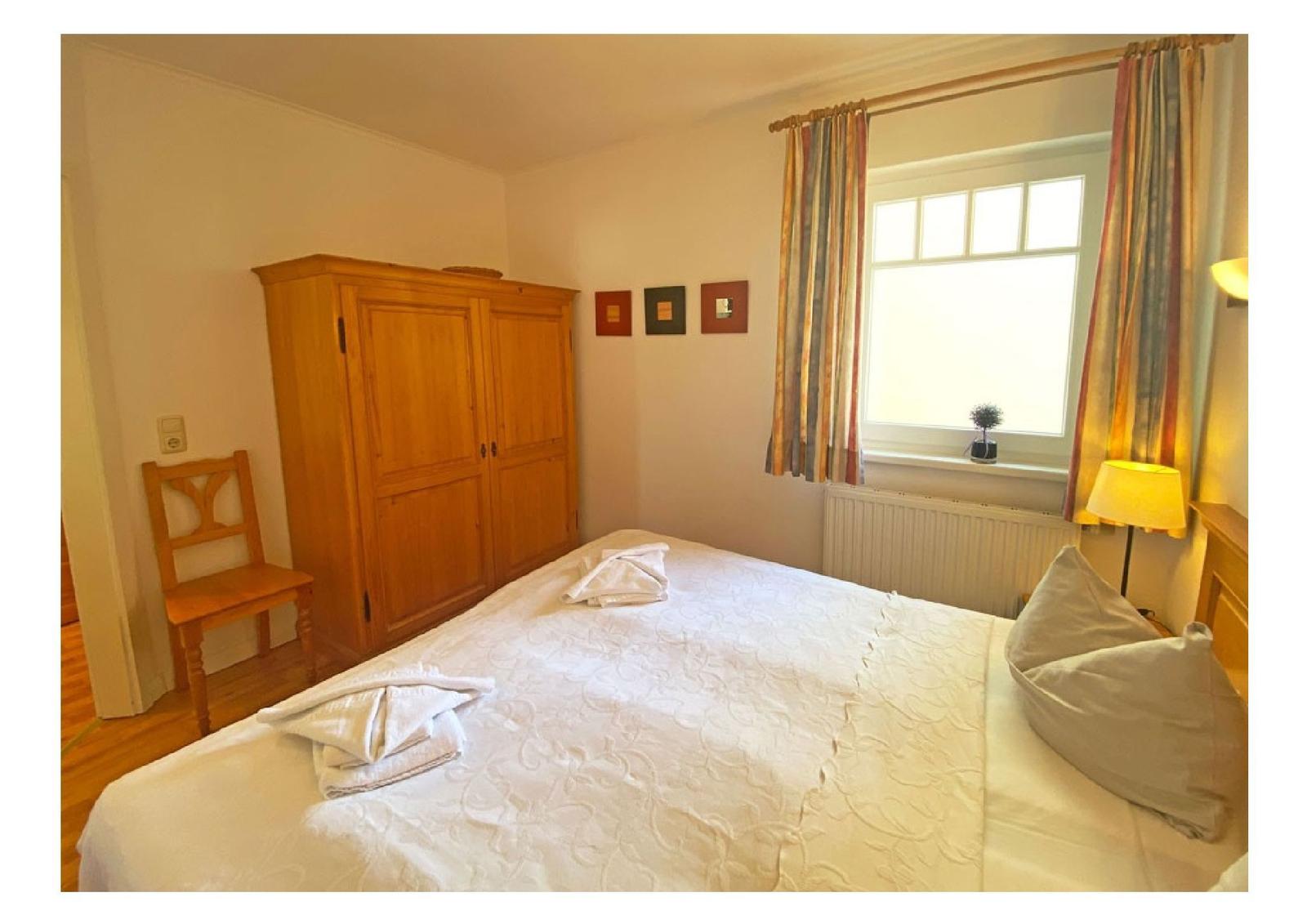 Schlafzimmer mit Bett, Holzschrank und Fenster mit Vorhängen.