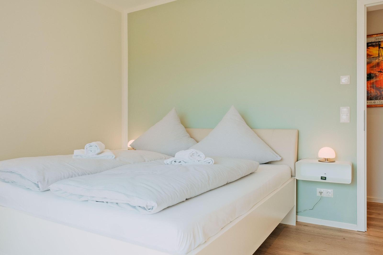 Schlafzimmer mit Doppelbett, weißen Bettwäsche und Nachttisch mit Lampe.