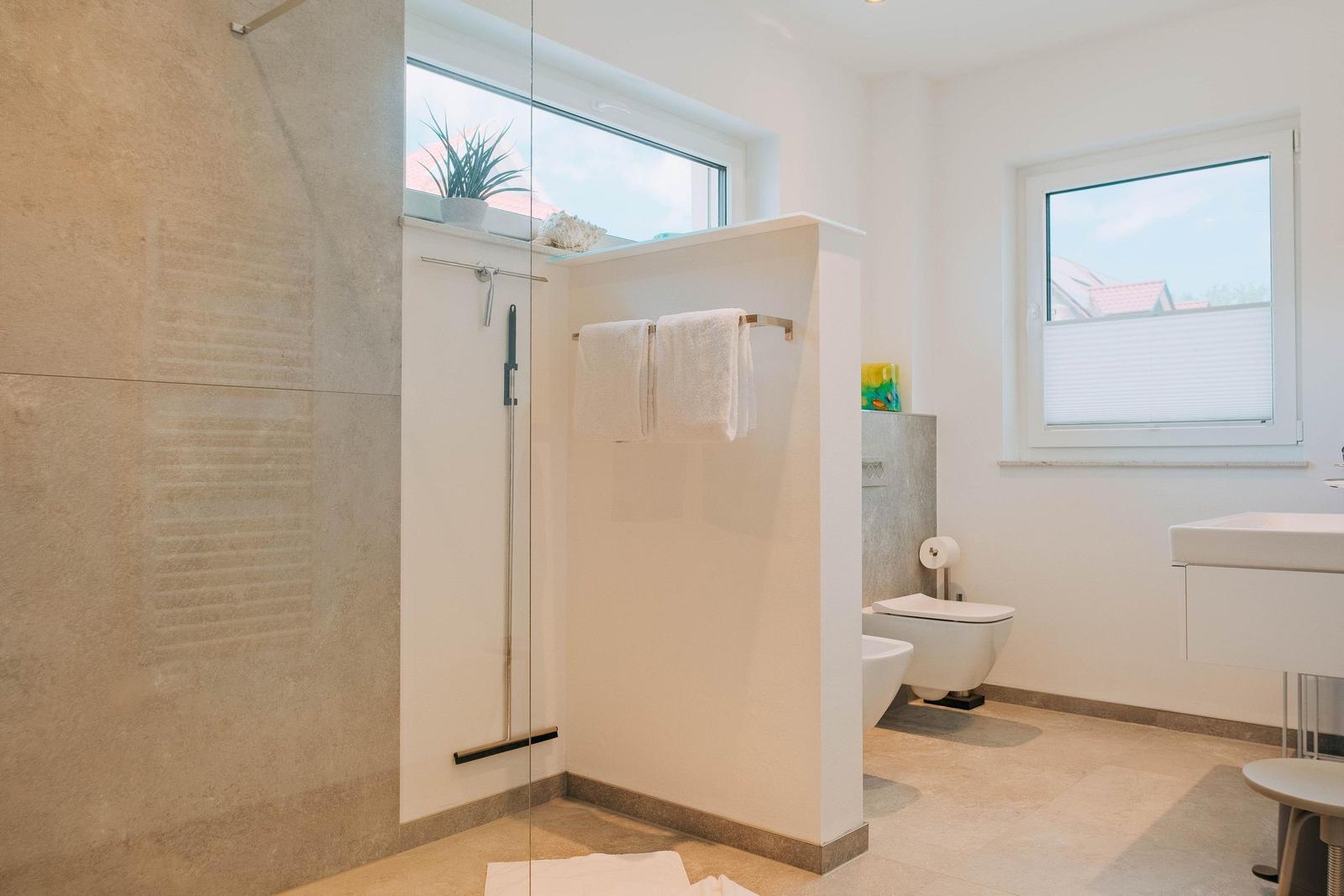 Badezimmer mit Dusche, Toilette und Waschbecken. Fenster mit Blick auf Dächer.