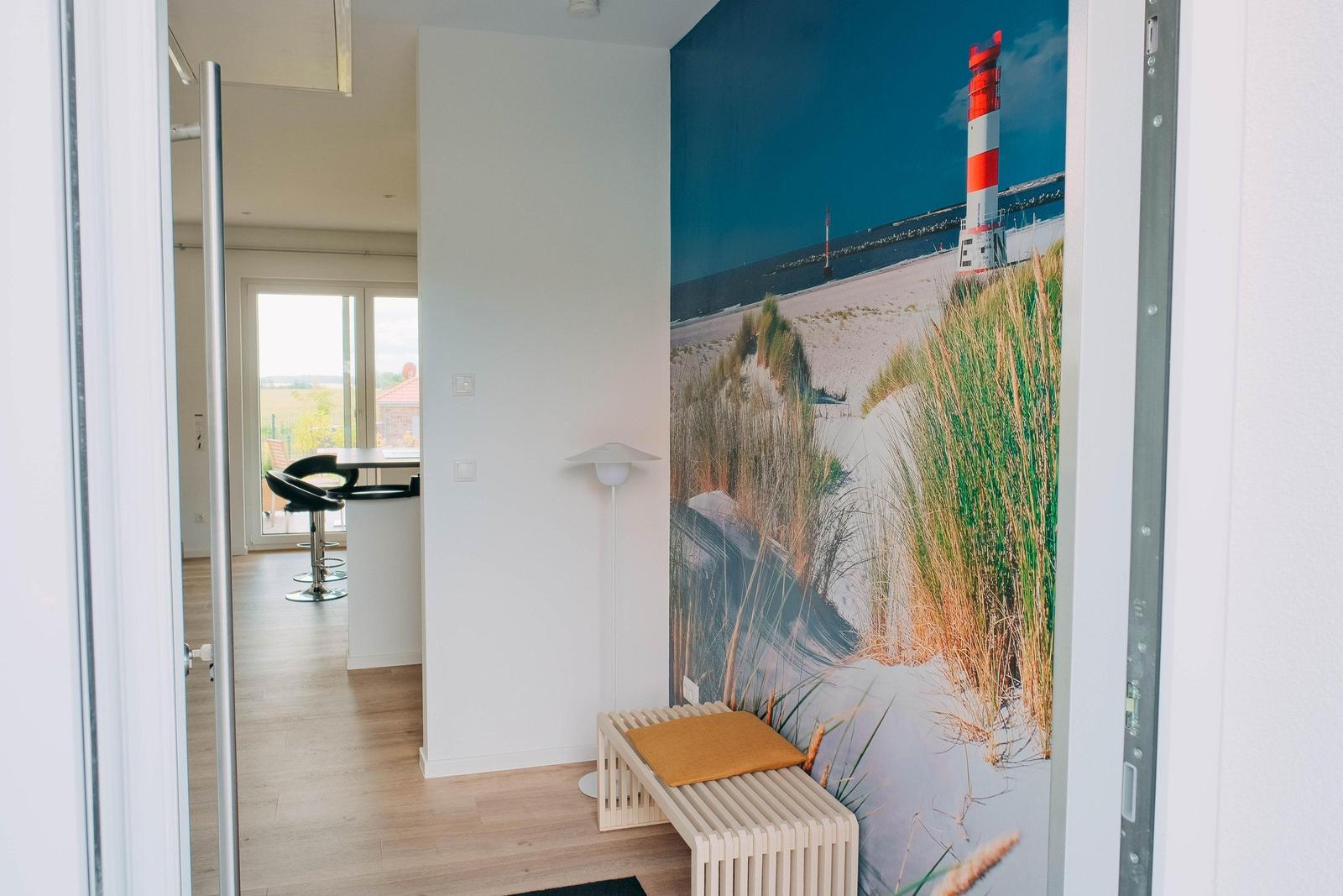 Eingangsbereich mit Wandbild eines Leuchtturms und Holzbank mit Kissen.
