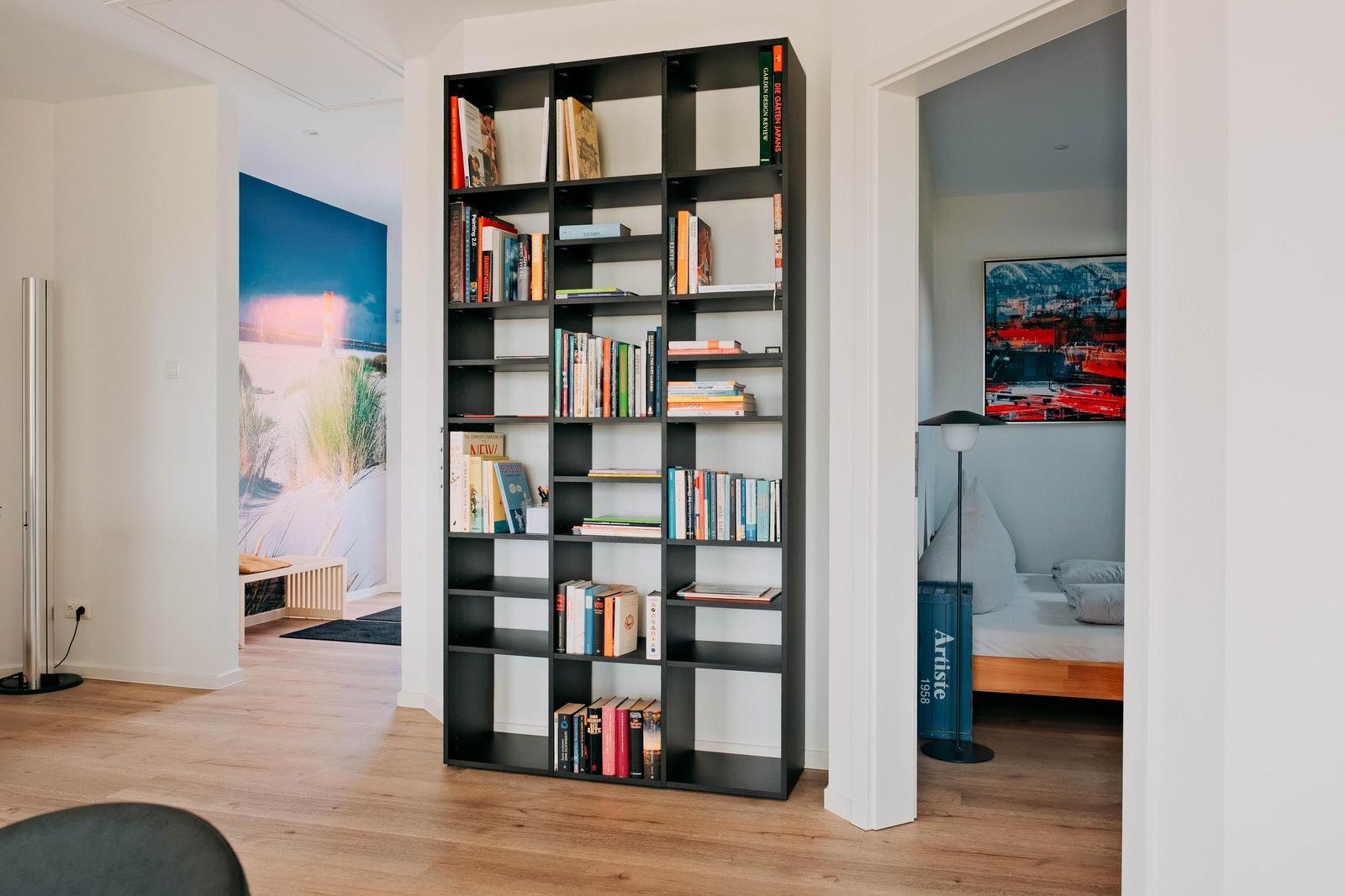 Großer Bücherregal trennt Wohn- und Schlafbereich. Schlafzimmer mit Bett und Wandbild.