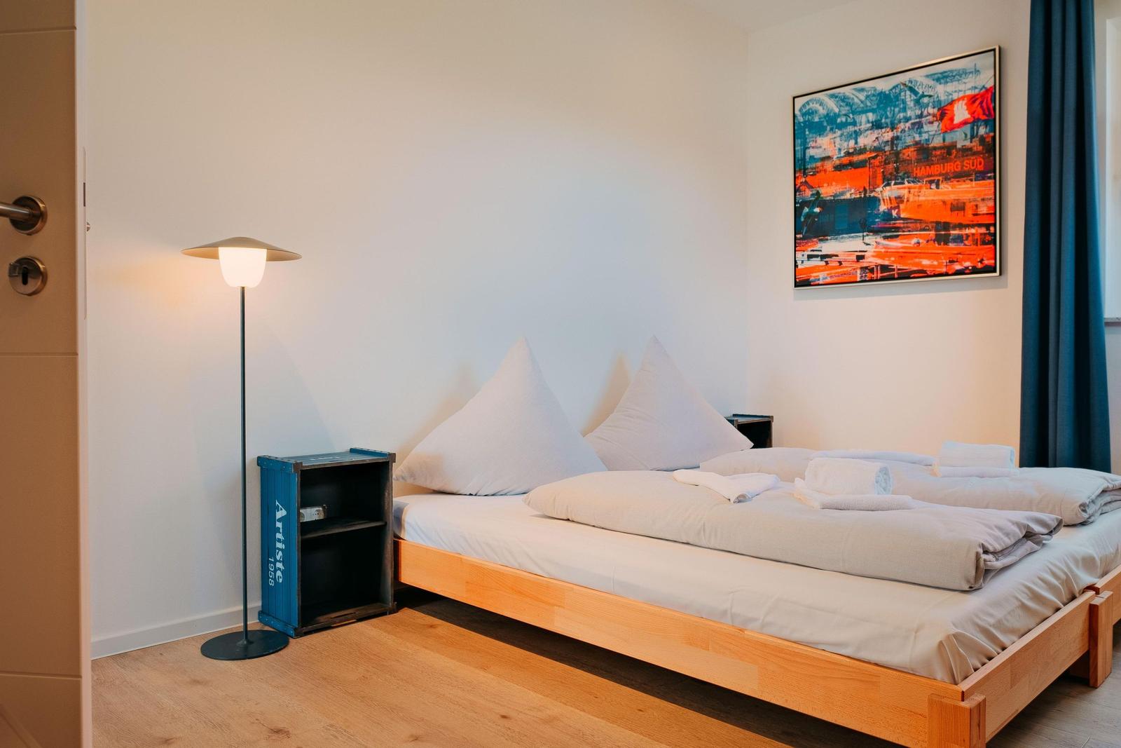 Ein Schlafzimmer mit Holzbett, blauer Gardine und Wandbild.