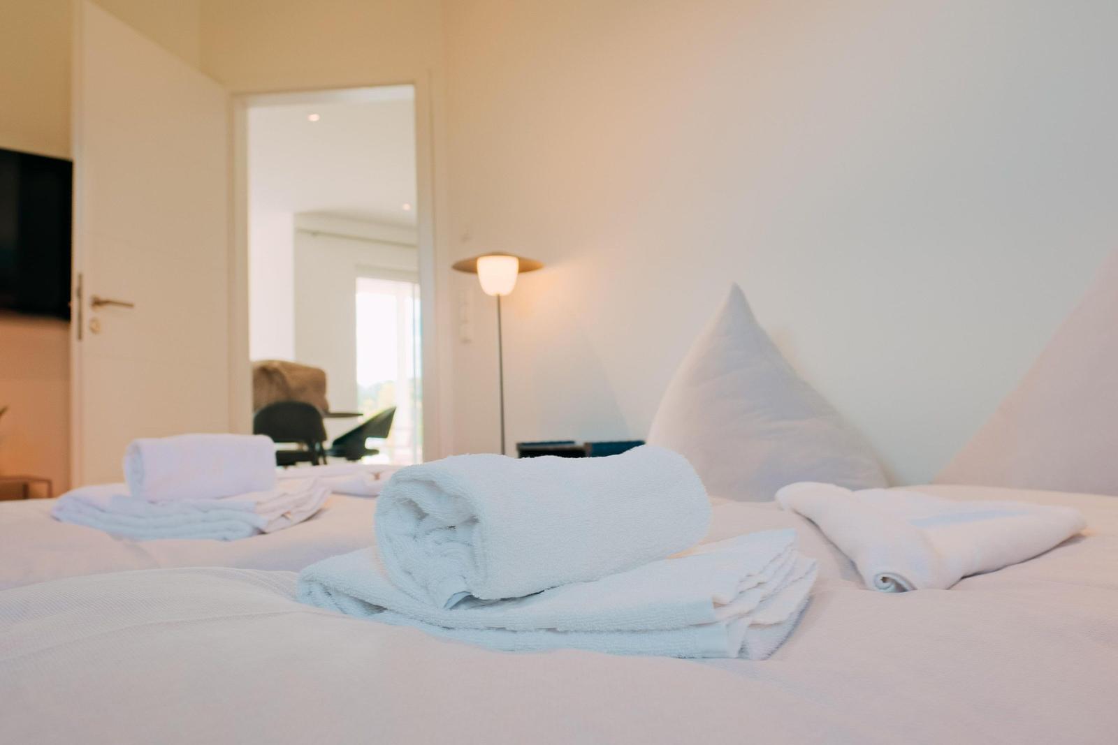 Ein Bett mit gefalteten Handtüchern und Kissen. Im Hintergrund ist ein Lampenlicht sichtbar.