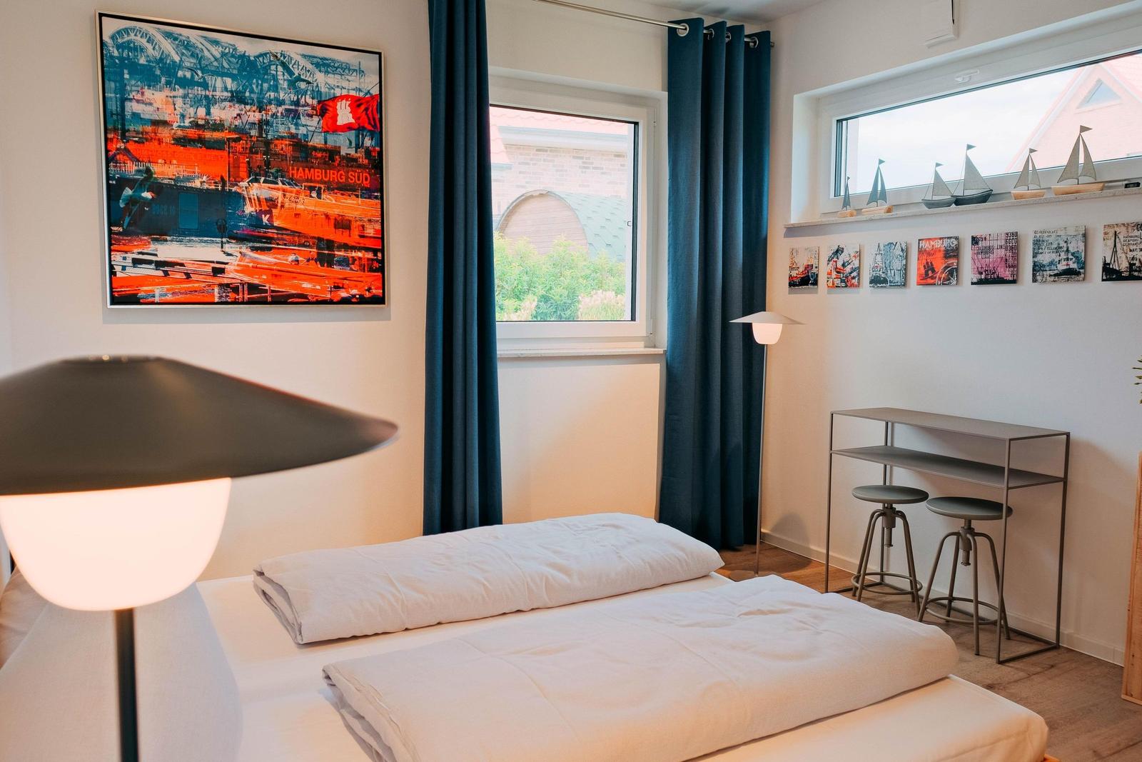 Schlafzimmer mit Bett, Fenster, Tisch und Wandbild.