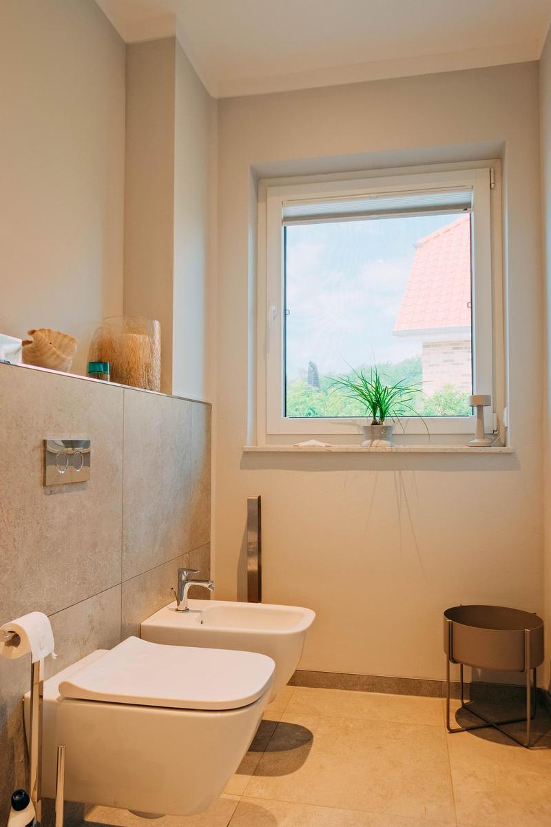 Badezimmer mit Toilette, Bidet und Fenster mit Blick auf Dach und Grün.