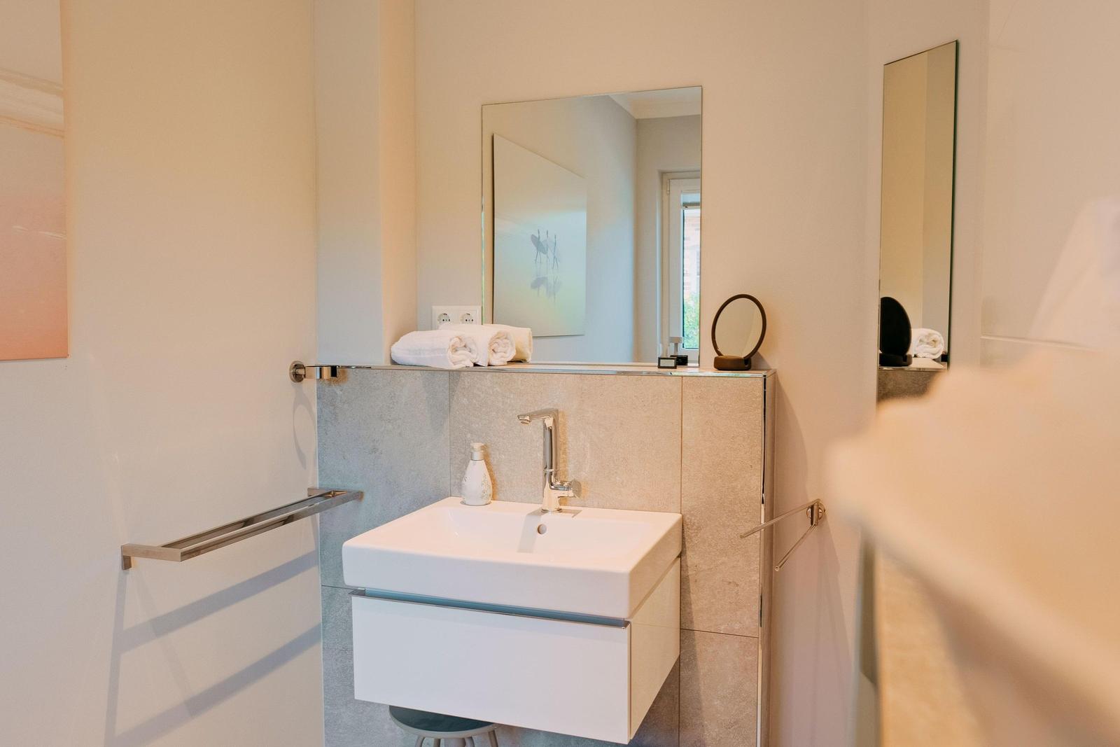 Badezimmer mit Waschbecken, Spiegel und Handtuchhalter.