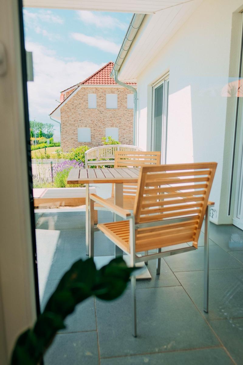 Terrasse mit Holztisch und Stühlen, Blick auf ein Haus und Garten.