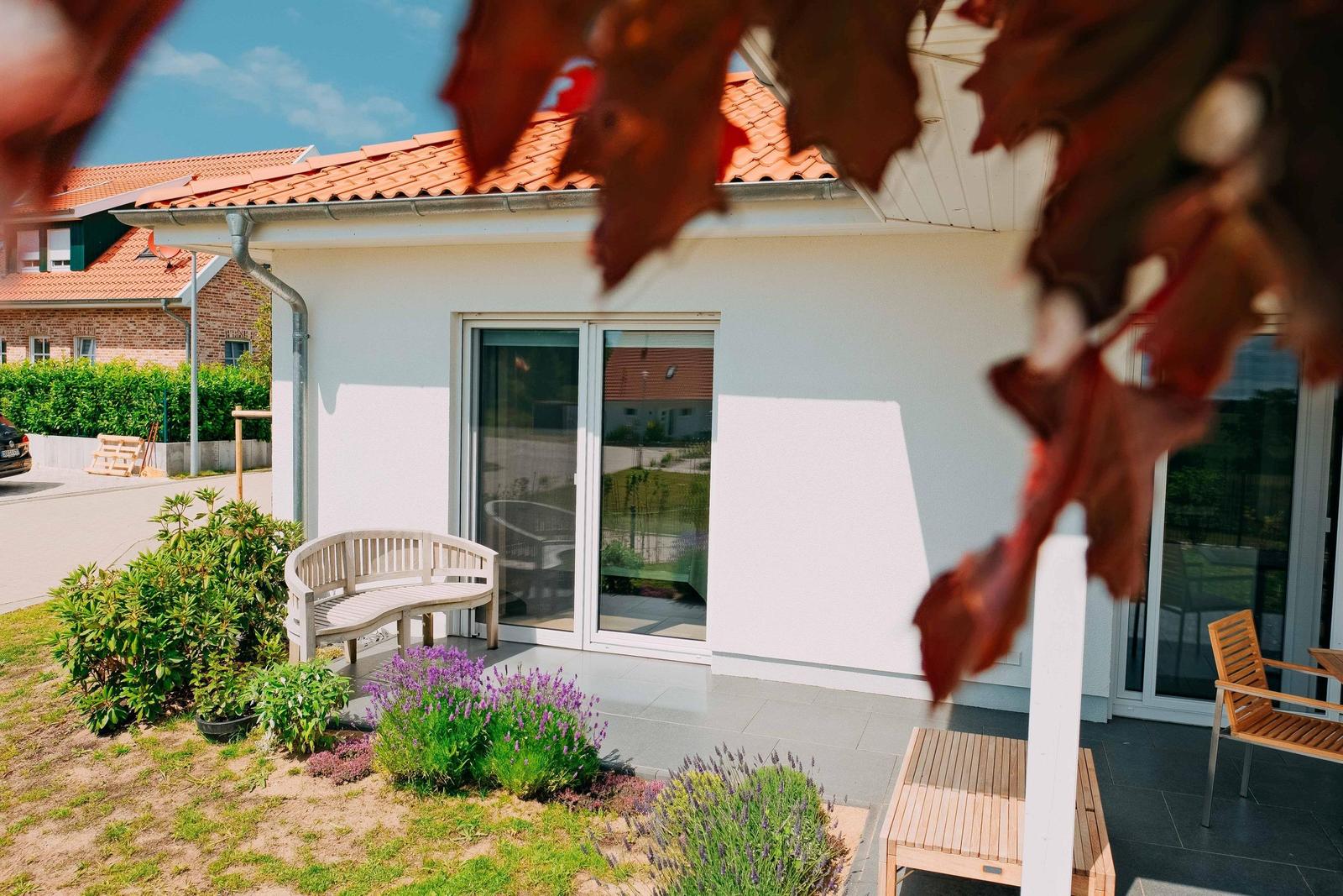 Wohnung mit Terrasse, Sitzgelegenheiten und Blumenbeeten im Vorgarten.