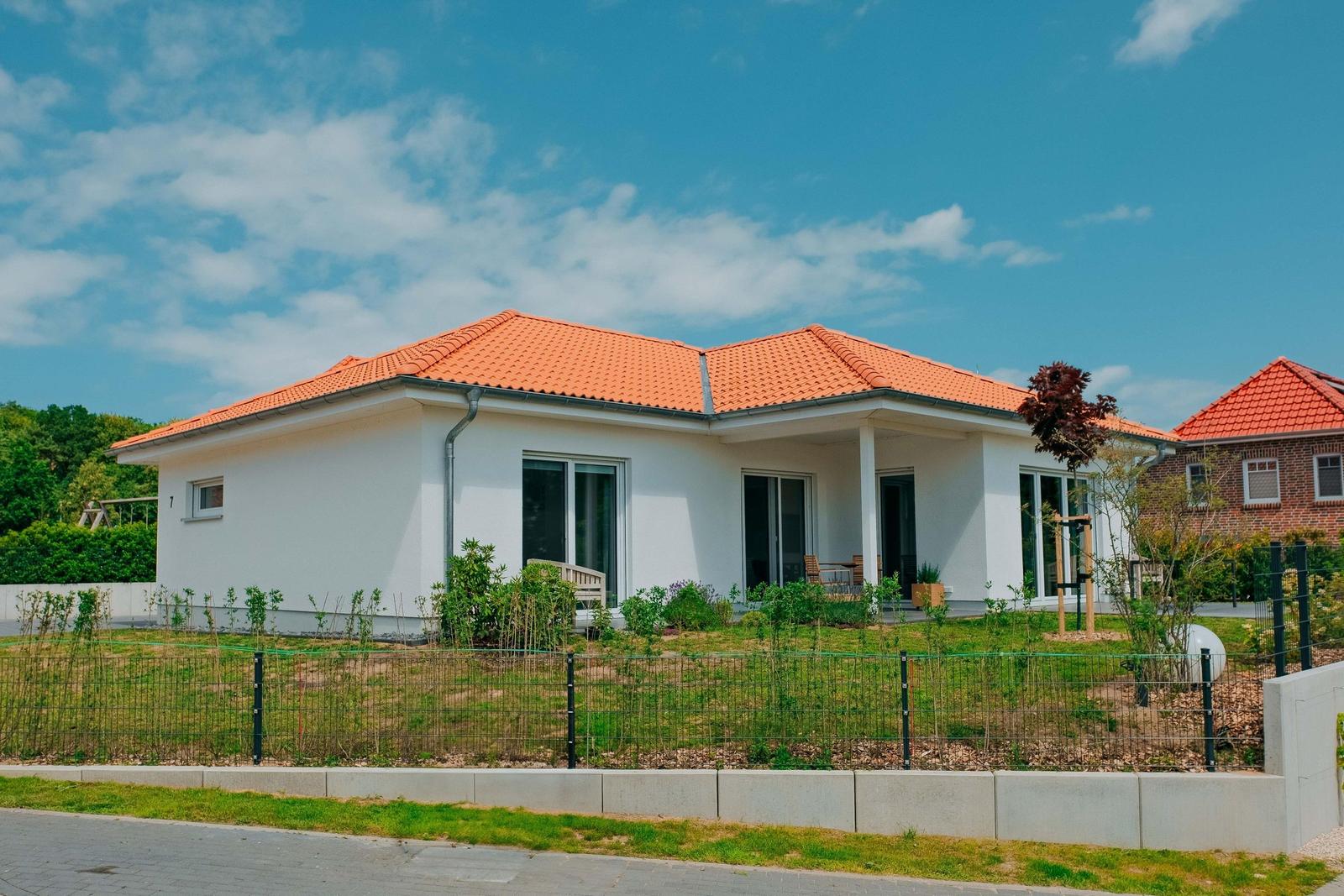 Modernes Haus mit orangefarbenem Dach und weißer Fassade. Gartenbereich mit Zaun und Sitzgelegenheit.