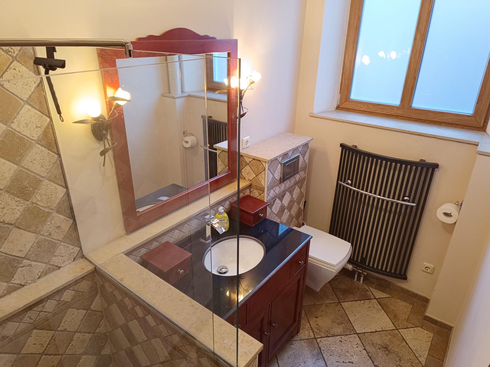 Badezimmer mit Waschbecken, Spiegel und Toilette. Steinfliesen und Holzrahmen.