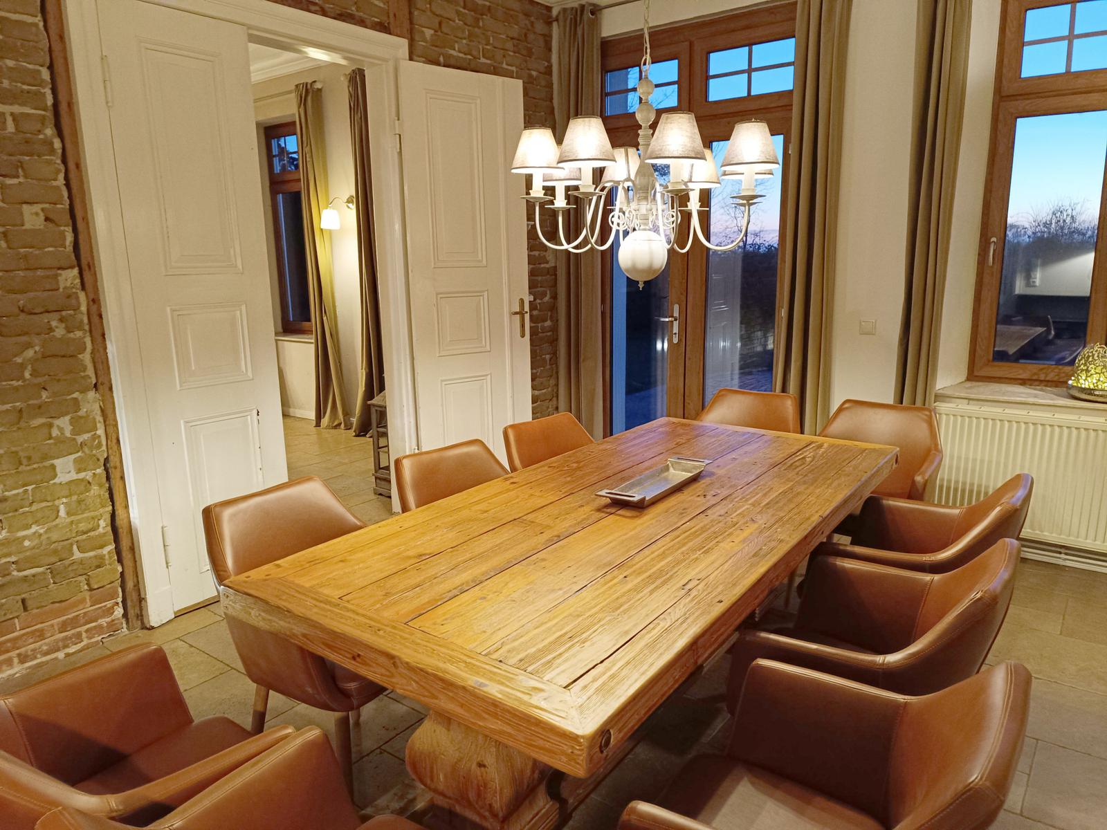 Esszimmer mit massivem Holztisch und Ledersitzen unter Kronleuchter.