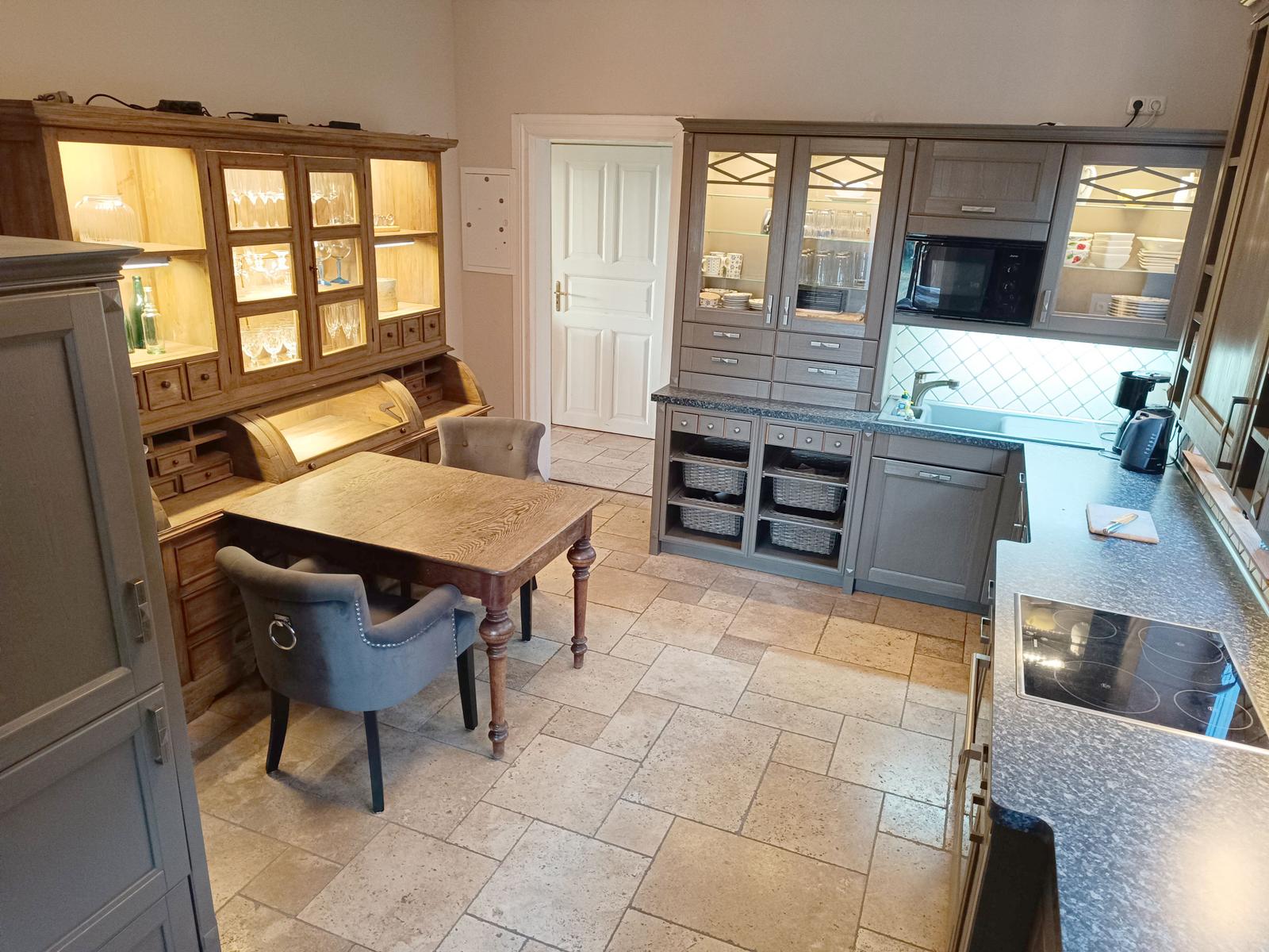 Küche mit Essbereich, grauen Schränken und Steinplattenboden.