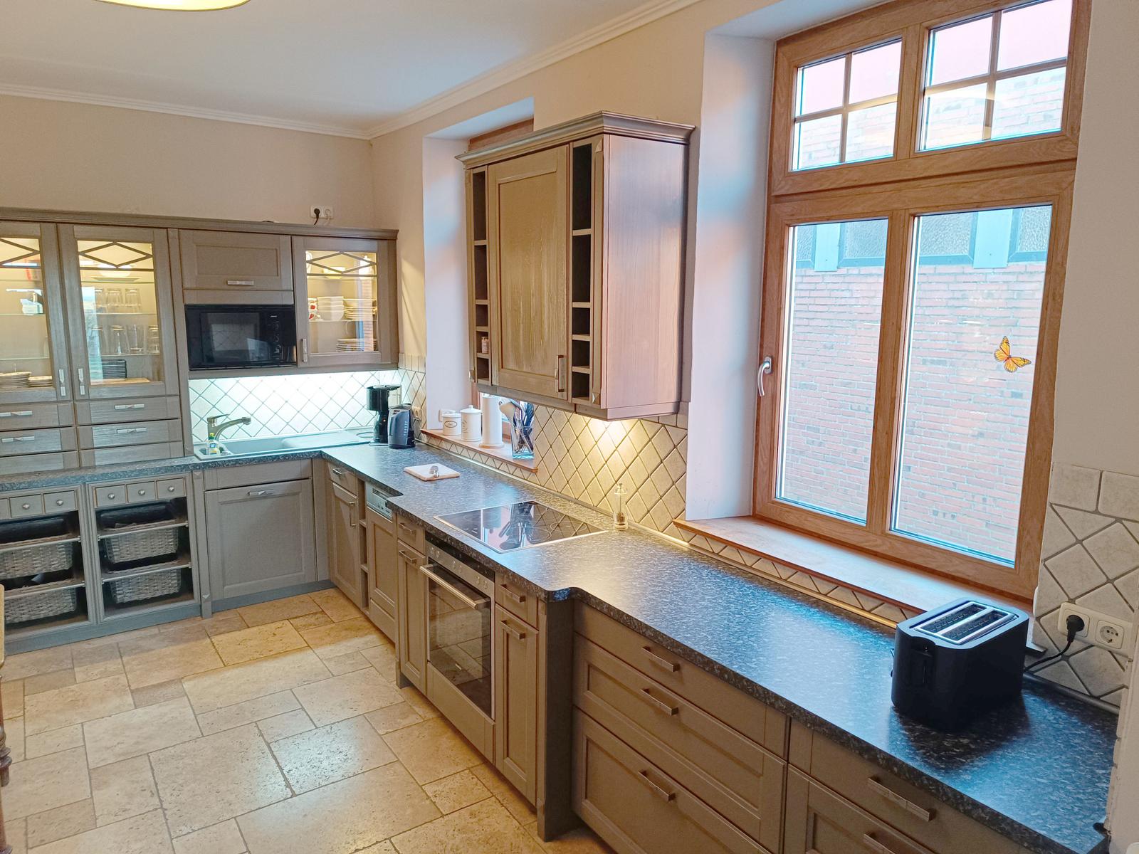 Küche mit Holzschränken, Arbeitsplatte und Fensterblick auf Backsteinmauer