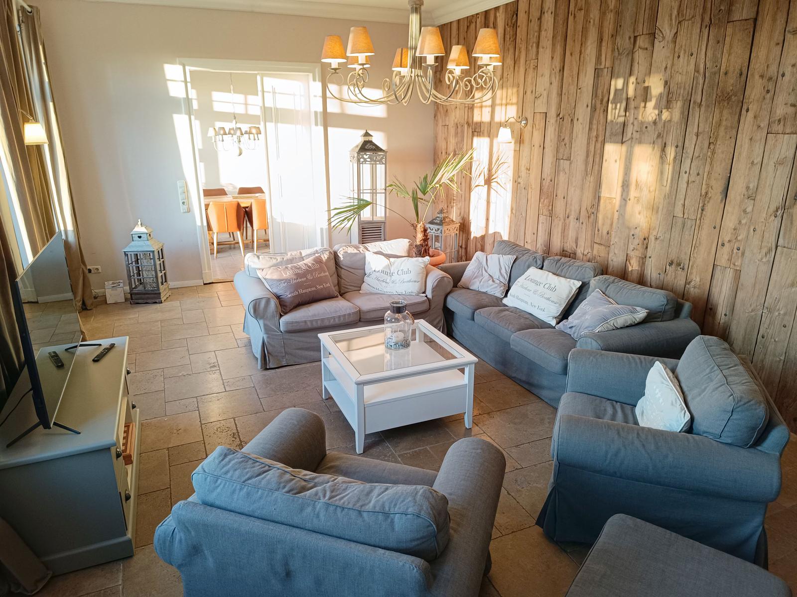 Wohnzimmer mit Holzwand, Sofa, Sessel und Couchtisch.