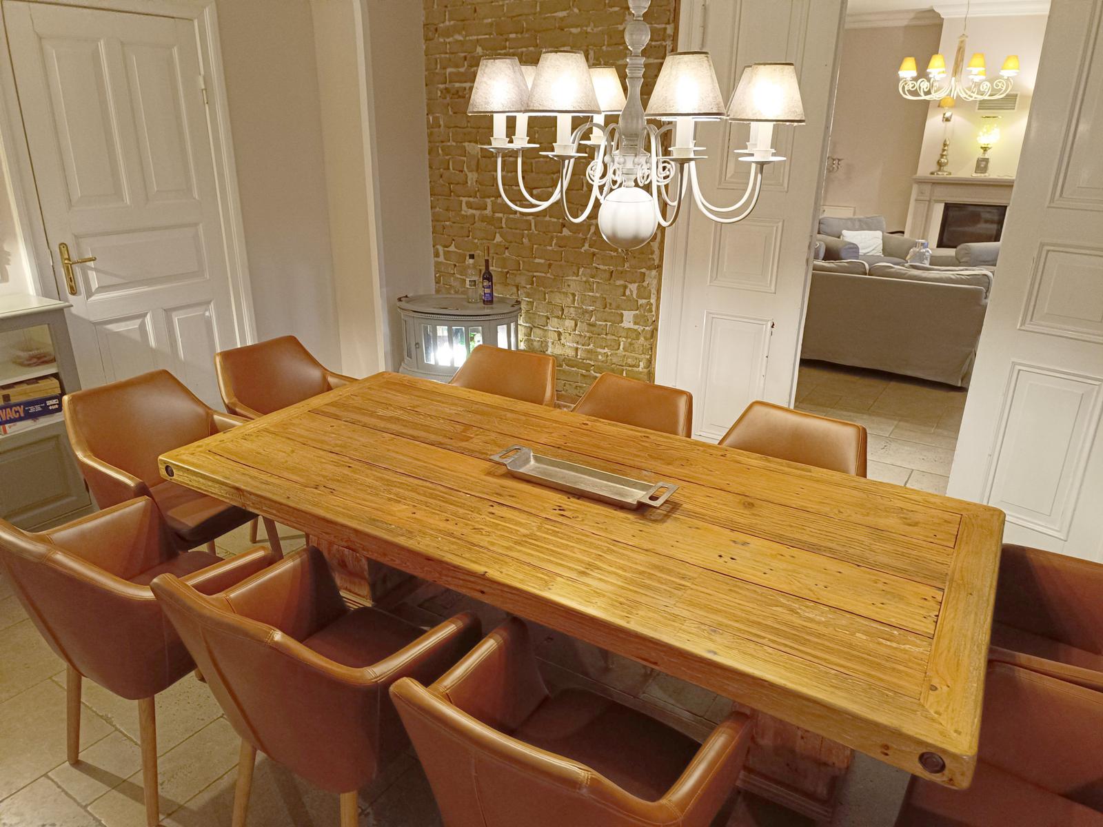 Holztisch mit sechs Ledersitzen unter einer weißen Pendelleuchte.