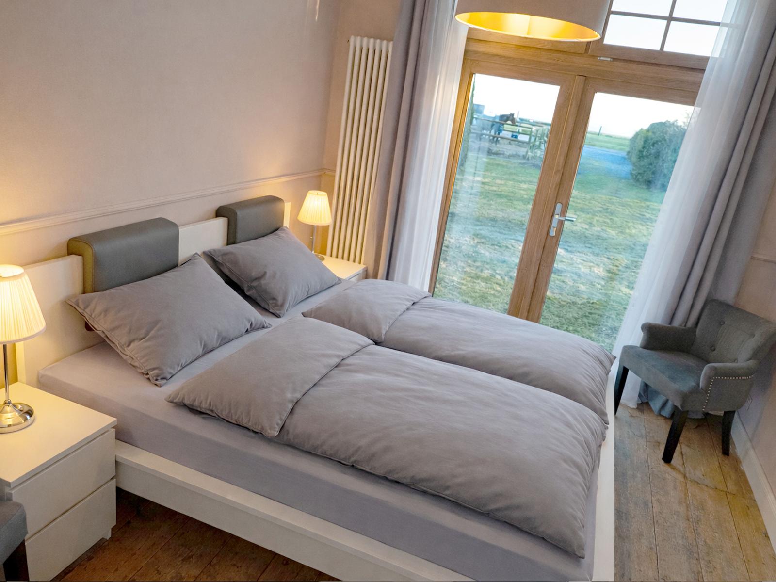 Schlafzimmer mit Doppelbett, Nachttischen und Sessel. Durchgangstür zur Terrasse.