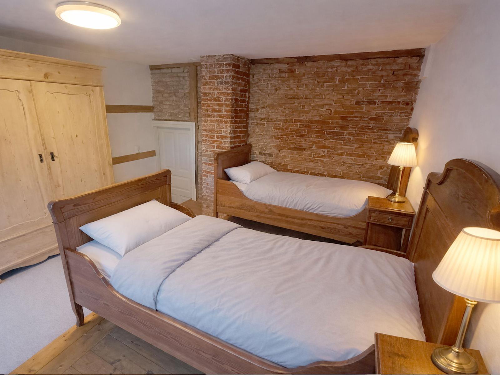Zwei Betten mit Holzrahmen und weißen Laken stehen in einem Raum mit Backsteinwand.